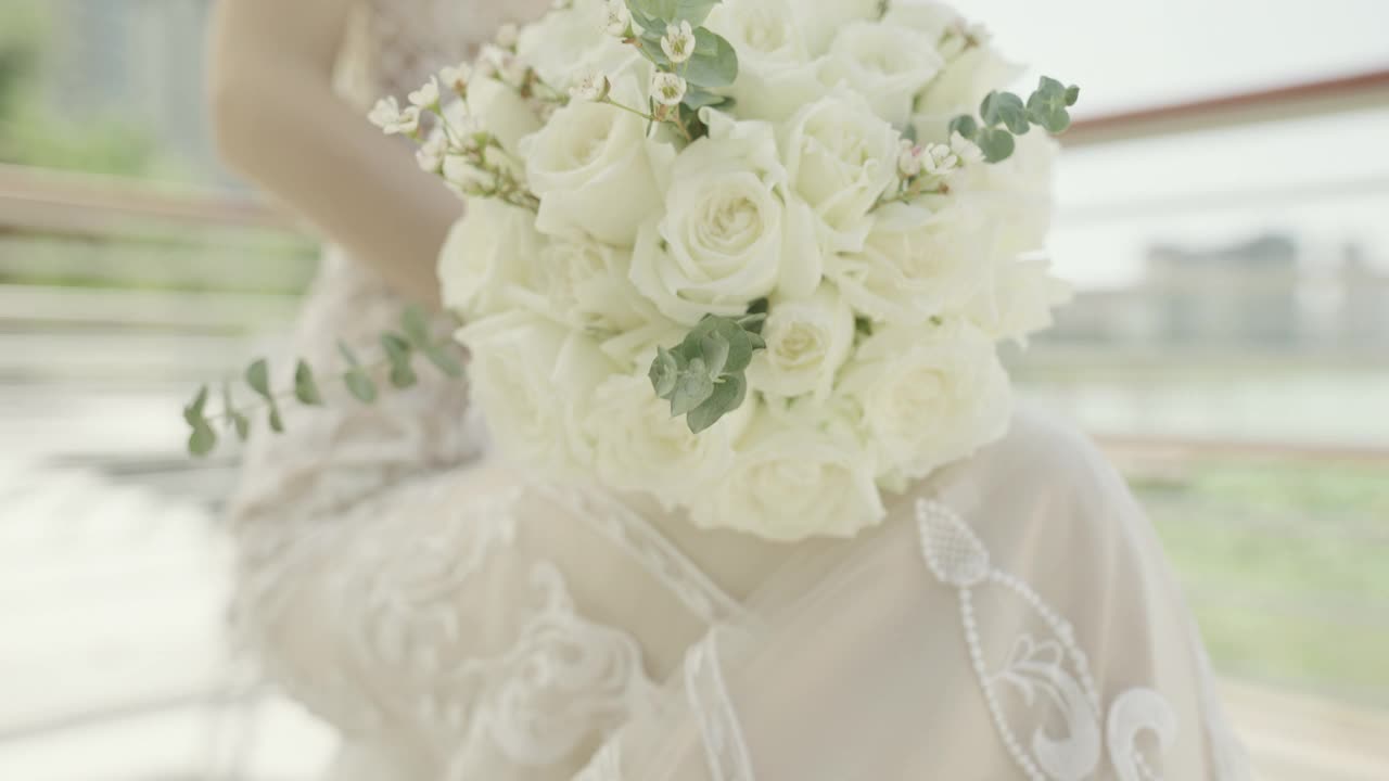 一个美丽年轻的亚洲新娘，手里拿着白色的鲜花，对着镜头微笑，中国新娘视频素材