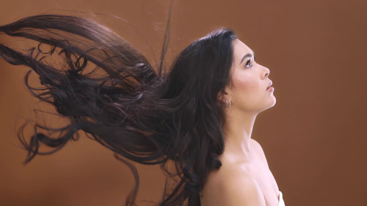 4k视频片段，一个迷人的年轻女子与她的头发吹在一个棕色工作室背景视频素材