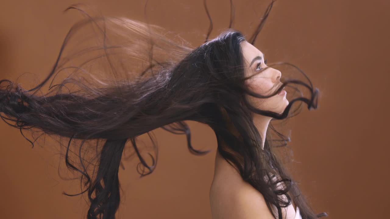 4k视频片段，一个迷人的年轻女子与她的头发吹在一个棕色工作室背景视频素材