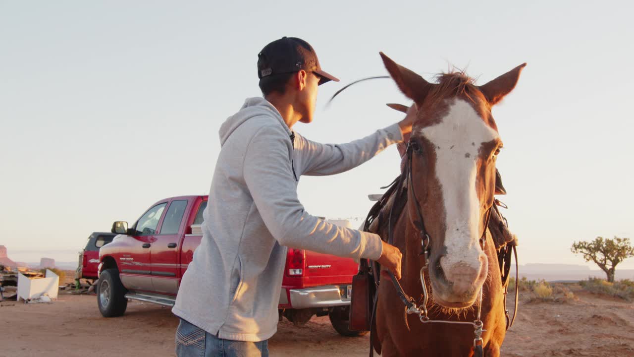 黄昏时分，美国土著纳瓦霍少年在亚利桑那州或犹他州纪念碑谷准备和骑上他的马视频下载