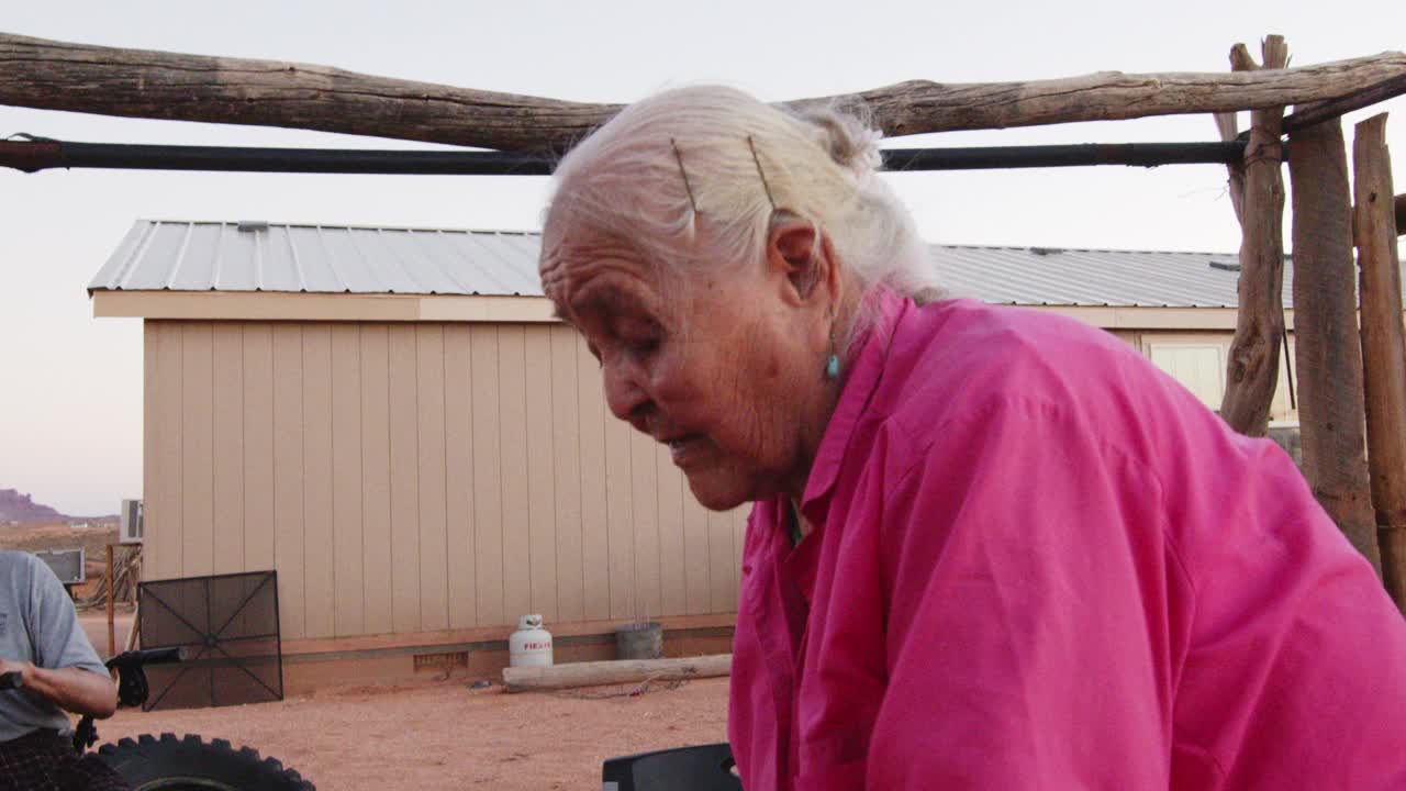 上了年纪的纳瓦霍妇女在她新编织的篮子上涂上松树树沥青，在室外的木炉子上取暖，她的丈夫和孙子看着她工作视频下载