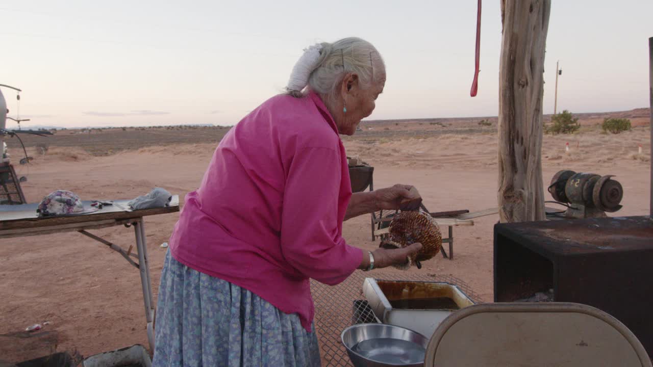上了年纪的纳瓦霍妇女在她新编织的篮子上涂上松树树沥青，在室外的木炉子上加热，特写视频剪辑视频下载