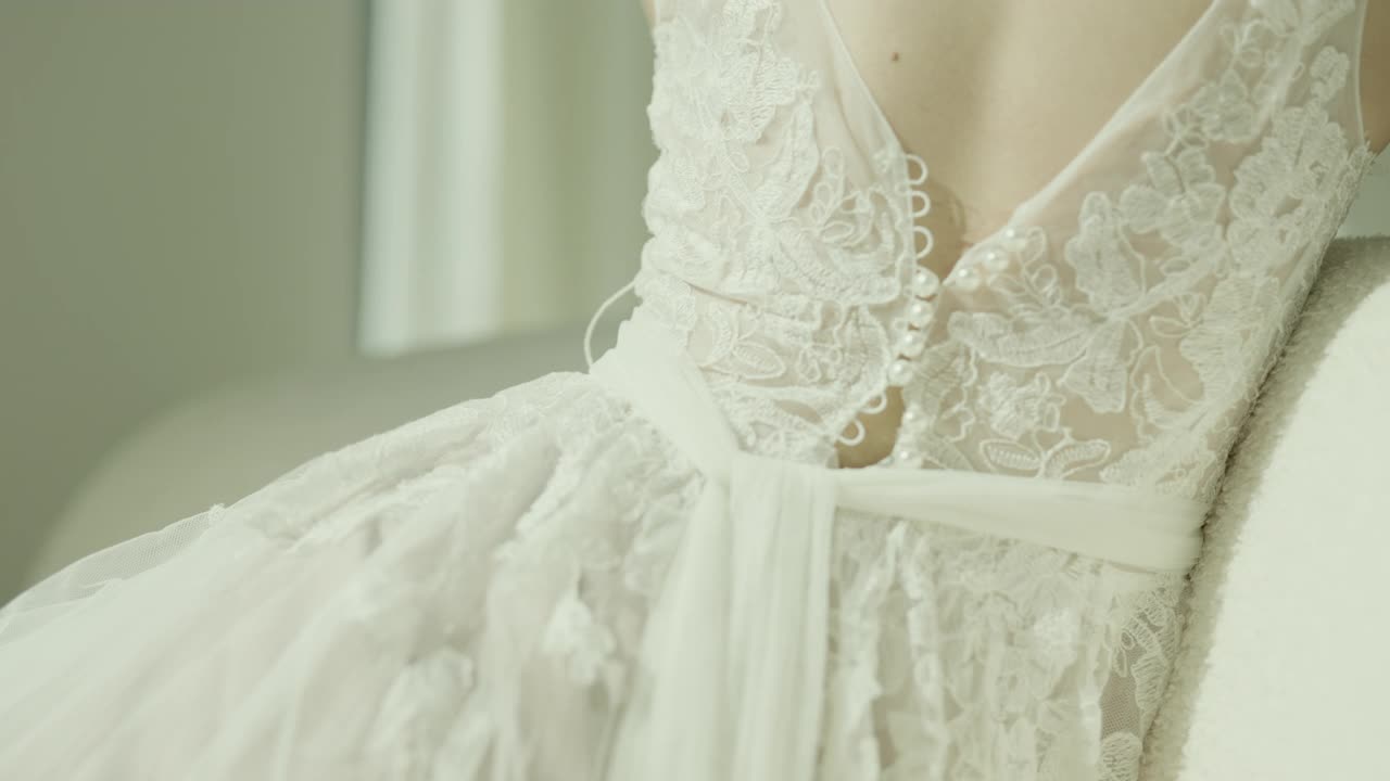 身穿白色婚纱的美丽亚洲新娘坐在落地窗前的沙发上慢镜头拍摄视频下载