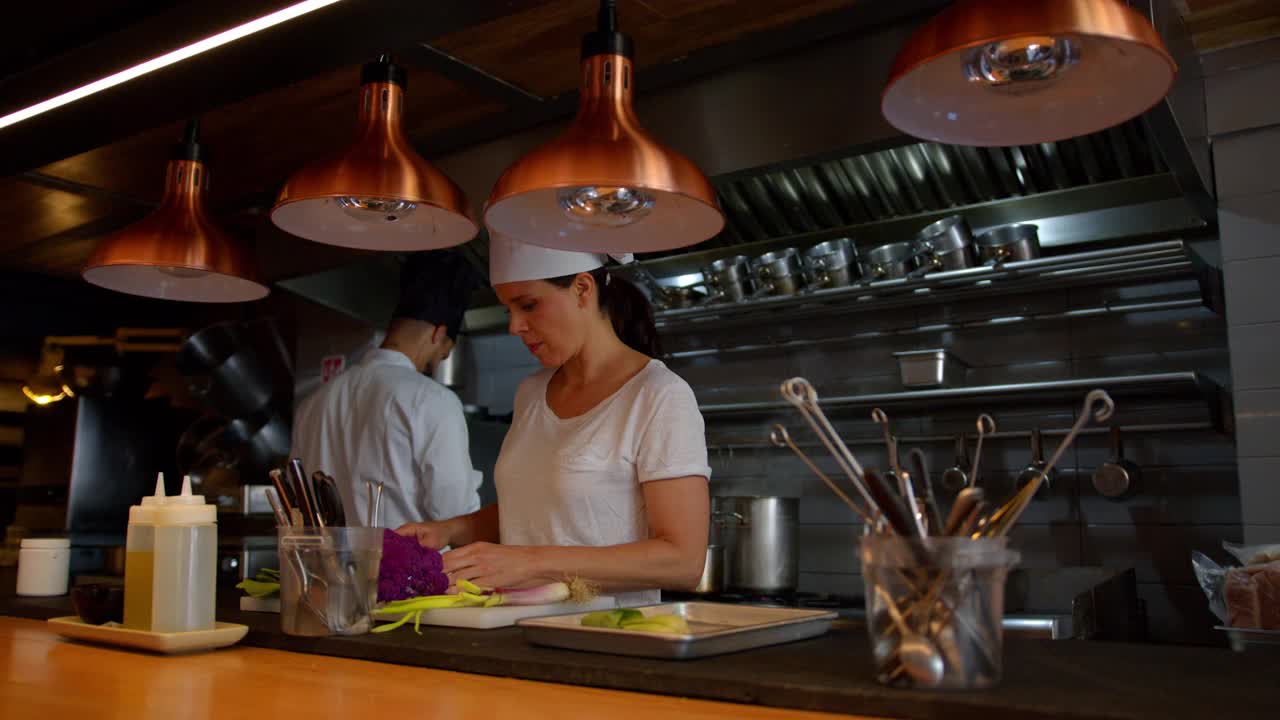 女副厨正在切菜，而厨师长则在一家gromet餐厅做背景工作视频下载