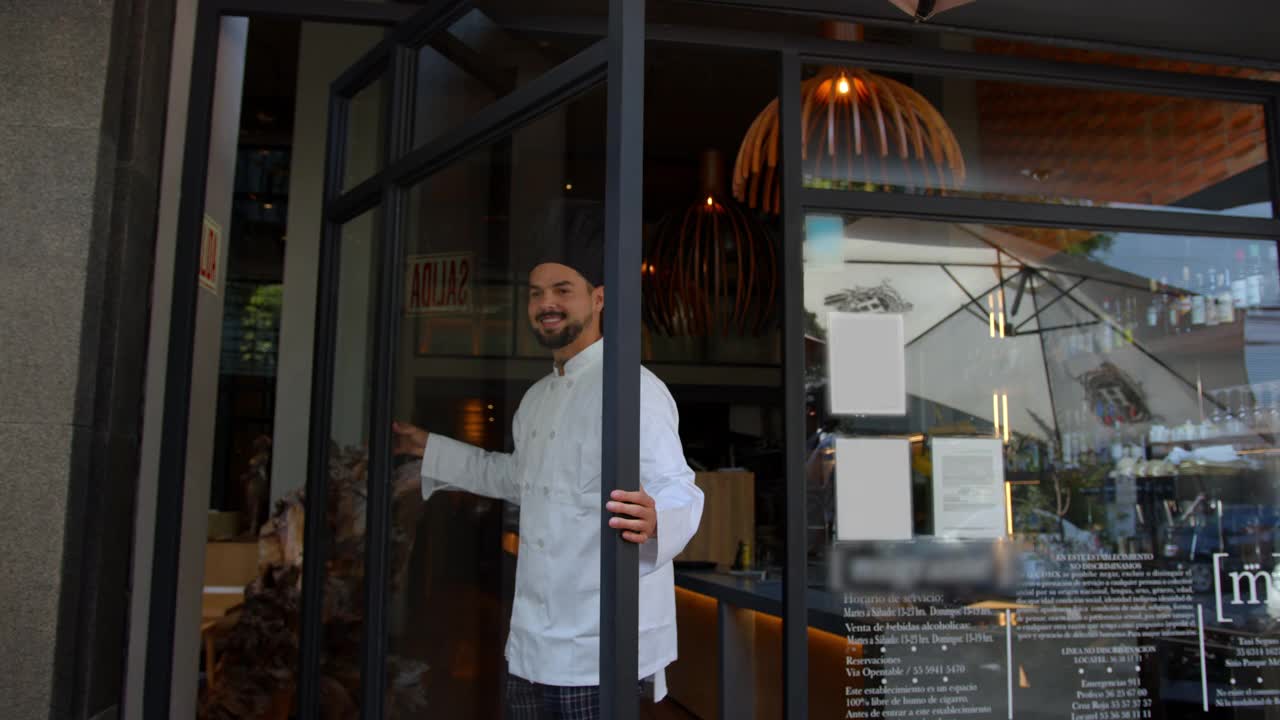 拉丁美洲英俊的餐馆老板打开门，对着镜头微笑，表示欢迎视频素材
