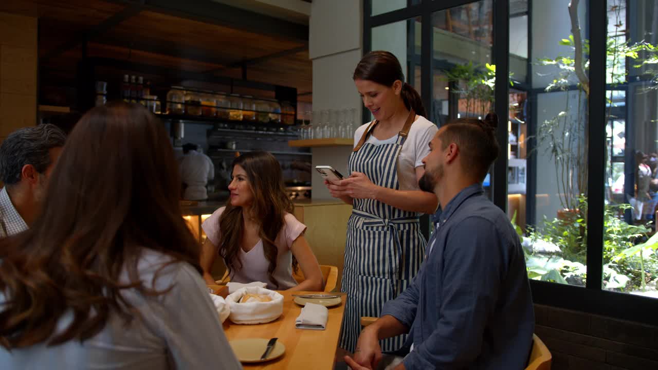一群朋友在餐厅点餐，友好的女服务员用智能手机帮他们点菜视频下载