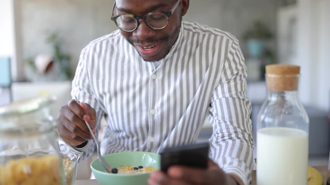 年轻人早上在家吃健康早餐，使用智能手机视频下载