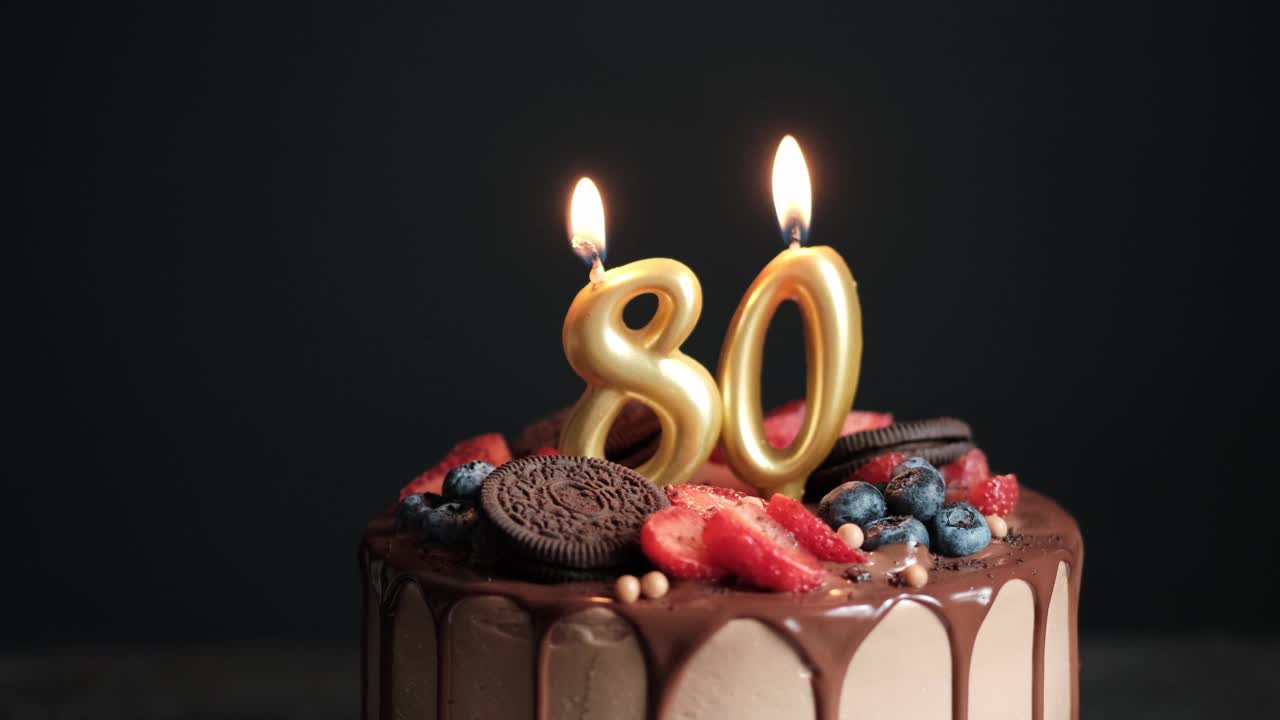 黑色背景的巧克力生日蛋糕和80号金色蜡烛。80周年的生日蛋糕。慢动作视频下载