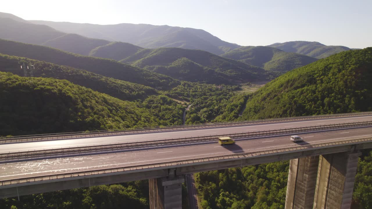 高架路鸟瞰图与卡车行驶在阳光明媚的绿色山丘视频素材