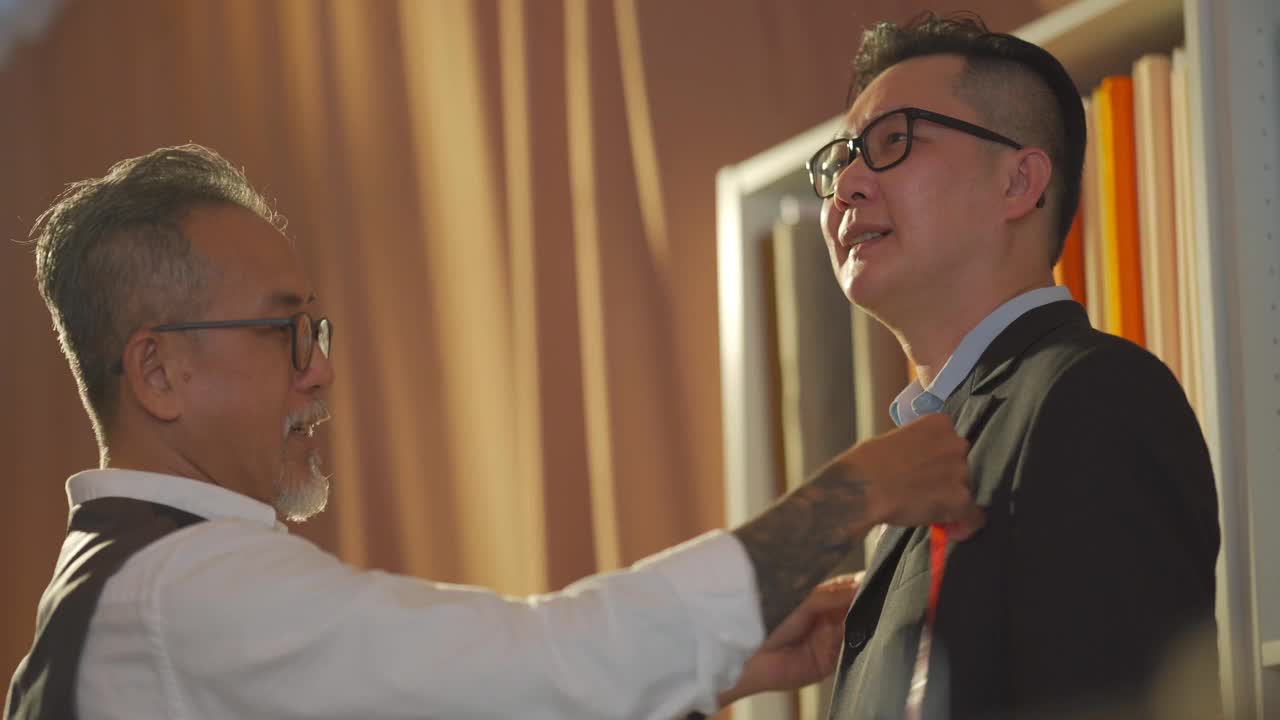 亚洲华人高级男裁缝用卷尺测量他的客户的身体尺寸为新的运动夹克在工作室制作，并写下数字平板电脑记录数字视频下载