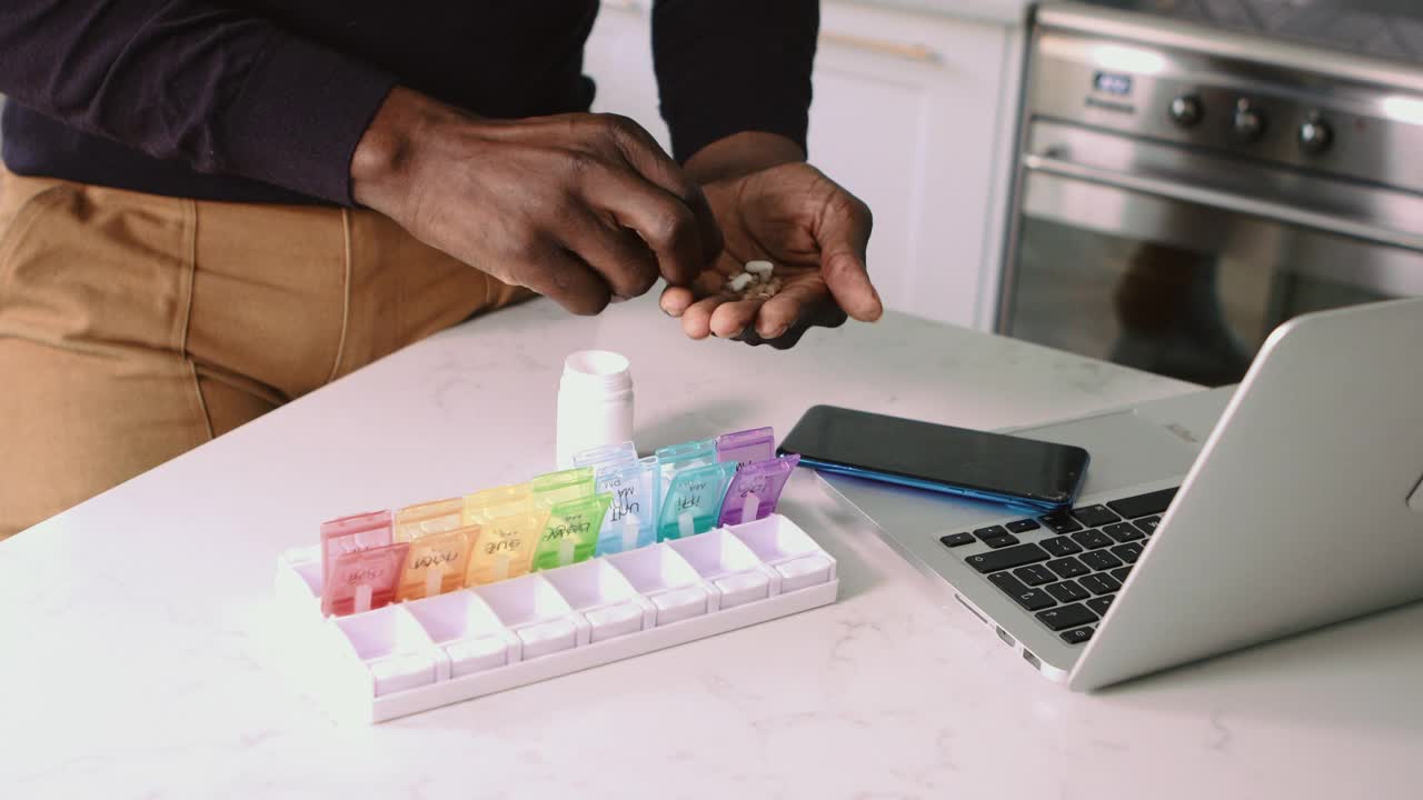 特写的黑人男子的手把处方药放在一个每日药片整理视频素材