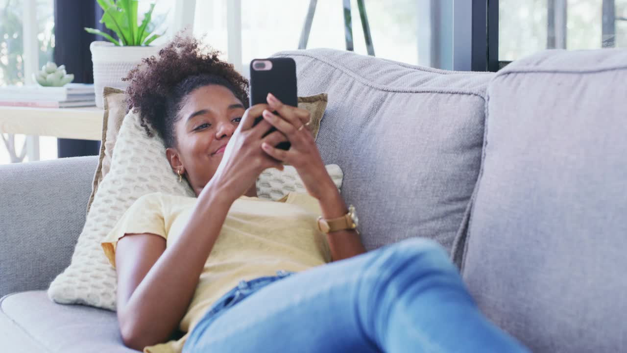 一名年轻女子在家里沙发上休息时使用手机的4k视频视频素材