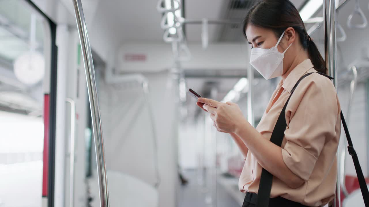 亚洲妇女戴着白色外科口罩，在地铁上使用手机视频素材