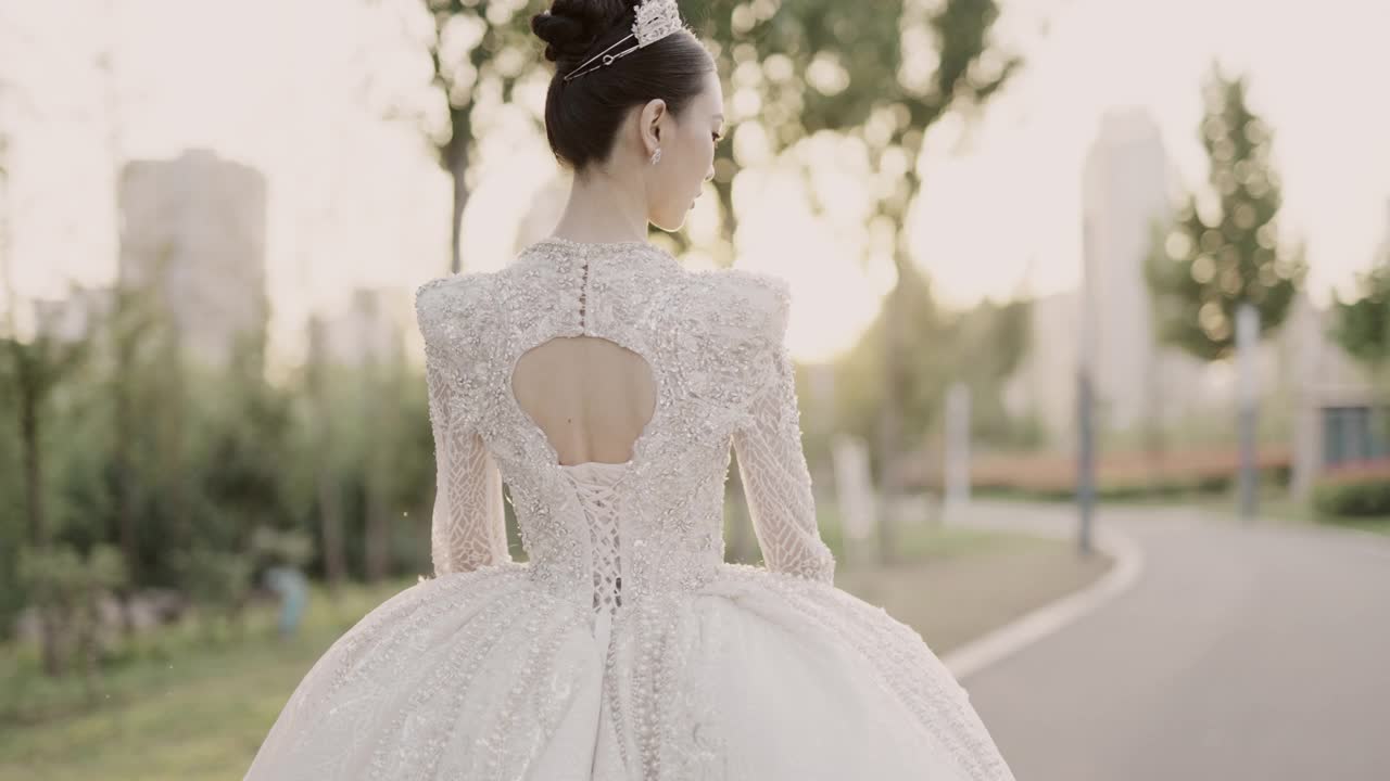 年轻美丽的亚洲新娘穿着白色婚纱，漫步在花园中，从后面拍摄，慢动作视频下载