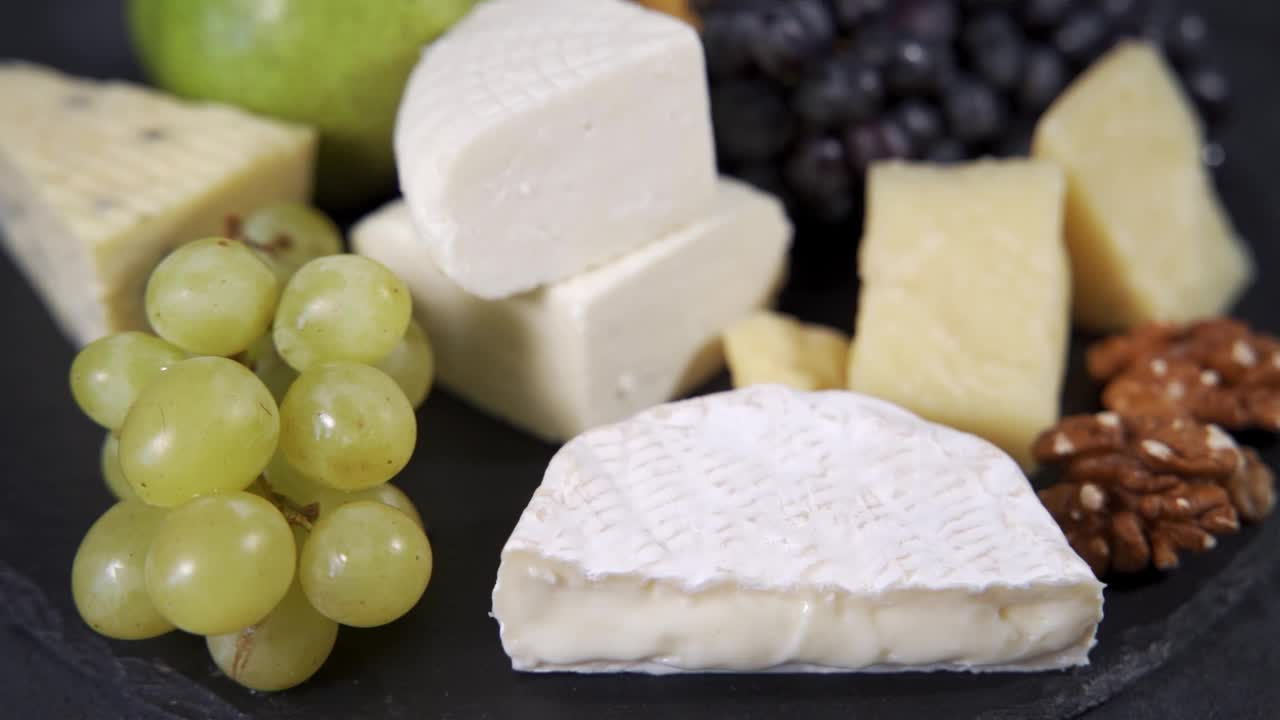 卡门贝尔奶酪旁边是绿葡萄、核桃和其他类型的奶酪。精选牛奶制成的美味昂贵的奶酪。视频下载