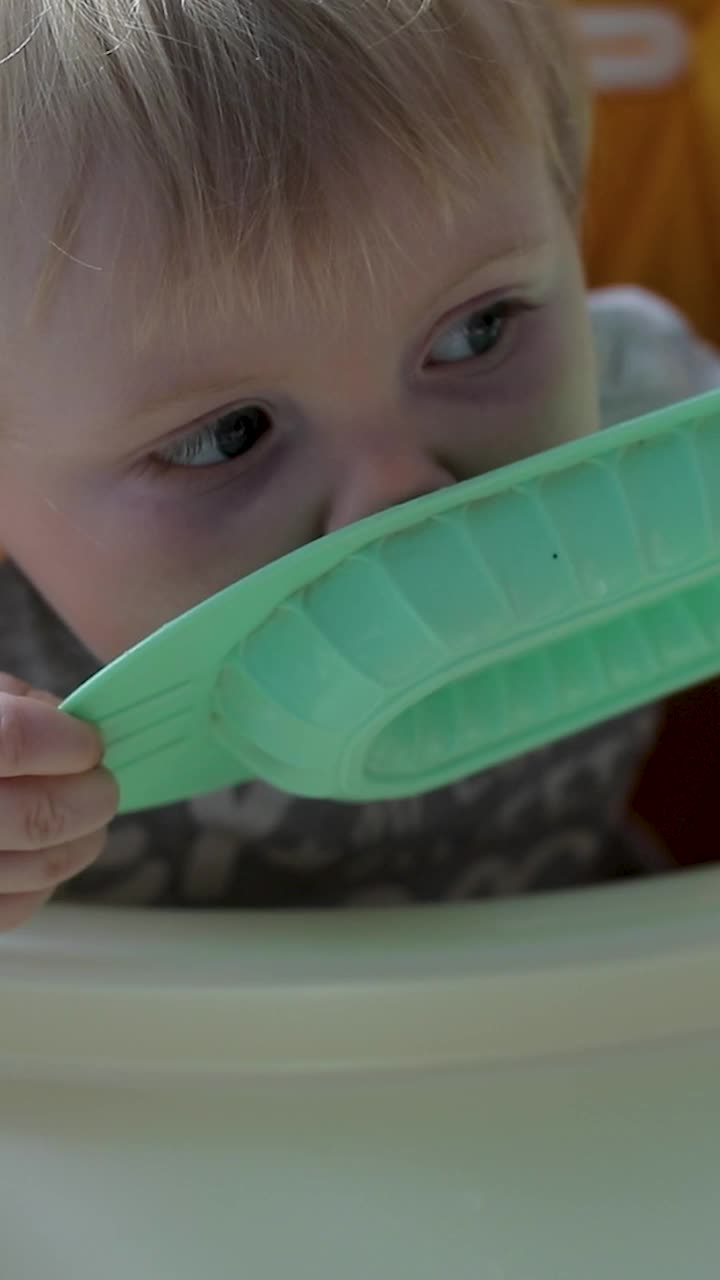 一个小孩子坐在高高的儿童桌旁舔着一个盘子。满脸都是粥视频素材