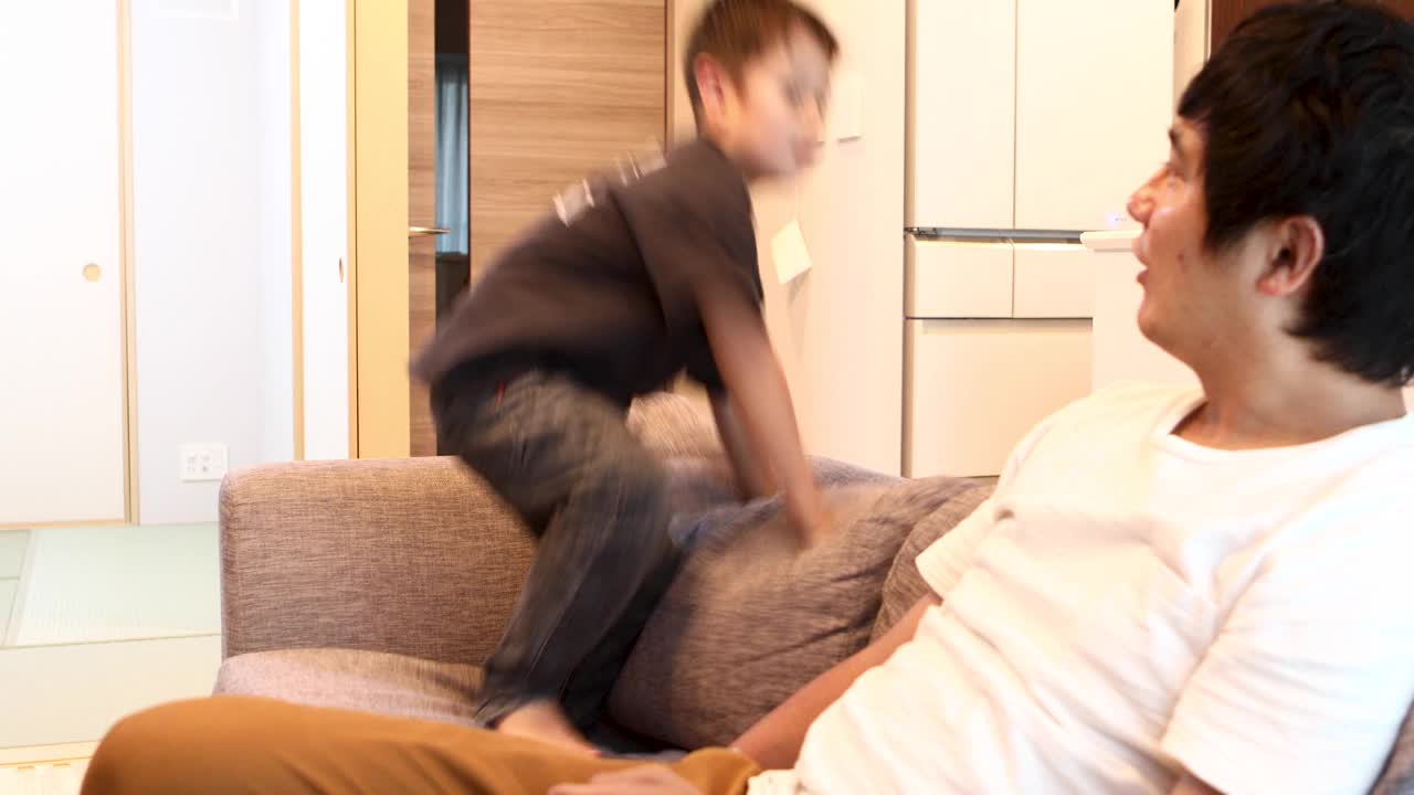 一位父亲沮丧地看到他的儿子在沙发上玩耍和跳跃时摔倒了视频下载