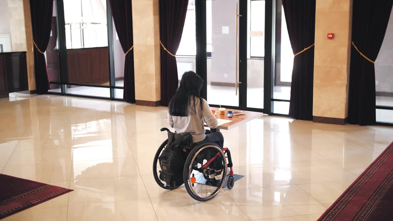 轮椅。残疾。残疾的年轻女子独自坐在轮椅旁画画。有残疾的人。教育、关系与人文观念视频素材