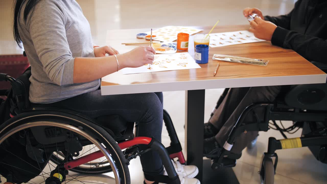 轮椅。残疾。特写镜头。残疾人坐在桌旁的轮椅上画画。为残疾人提供的创造性团体课程。教育、关系与人文观念视频素材