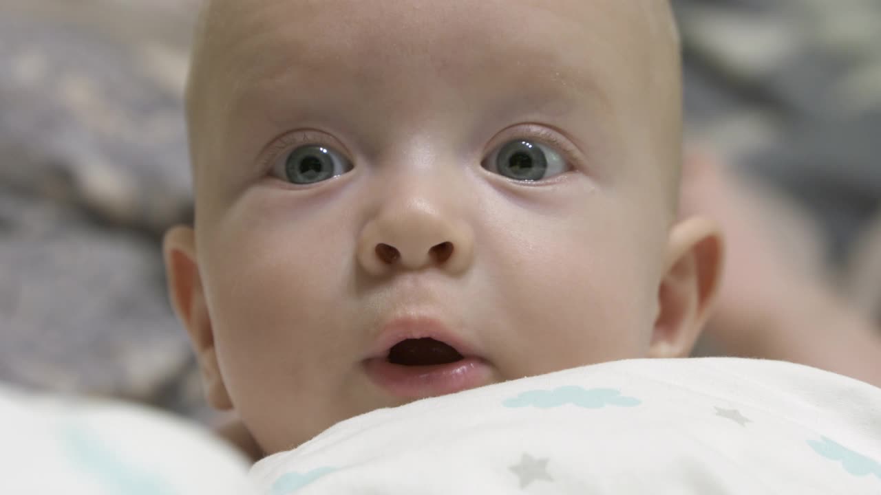 宝宝惊讶地看了看，可爱的宝宝躺在床上，脸朝着白种人六个月大的小男孩。视频素材