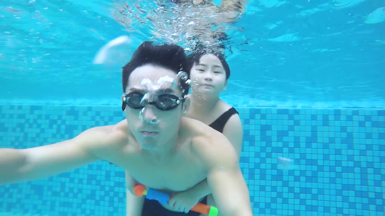度假期间，亚洲华人女儿抱着父亲在游泳池游泳。有问题。视频下载