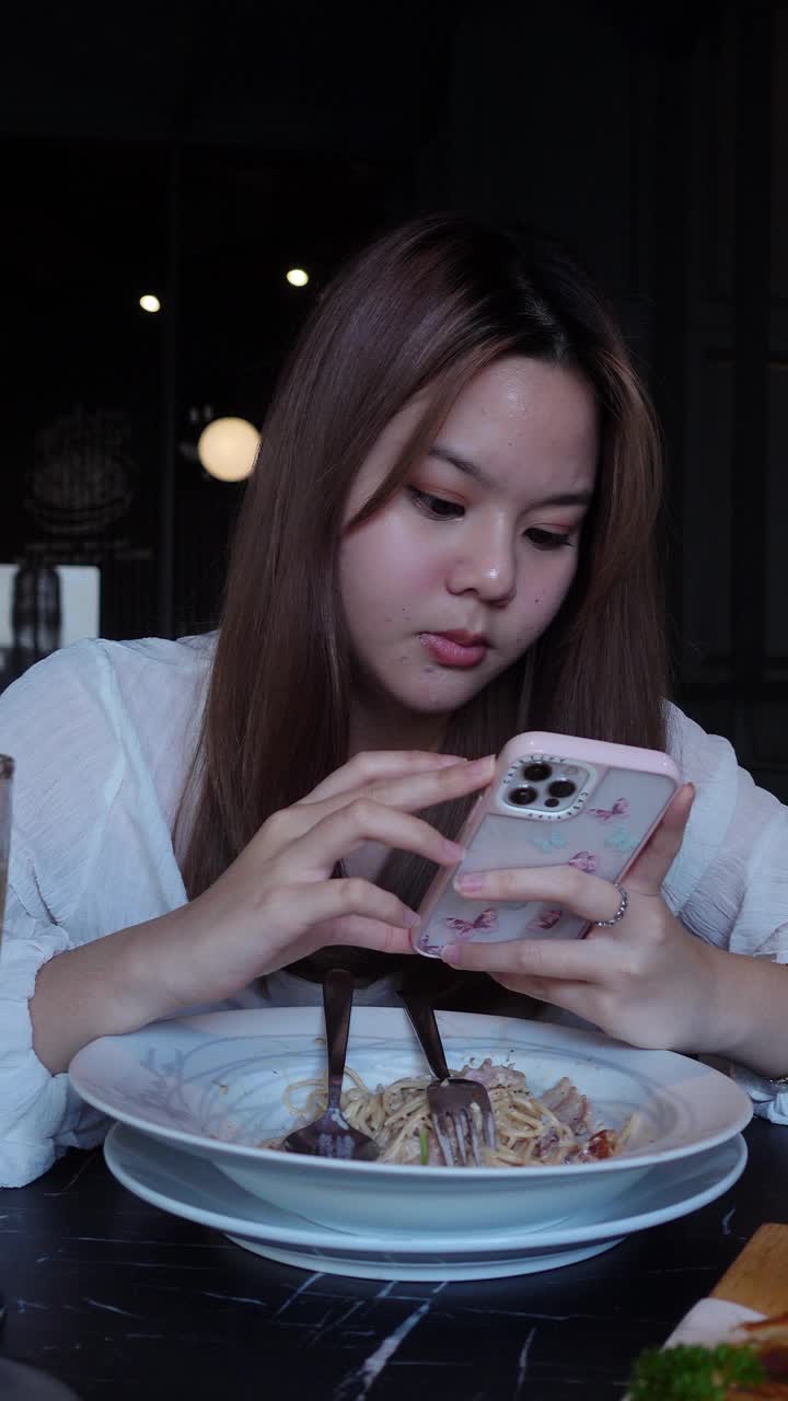 亚洲视频博主十几岁的女孩在餐厅吃饭时用智能手机拍照或视频视频下载