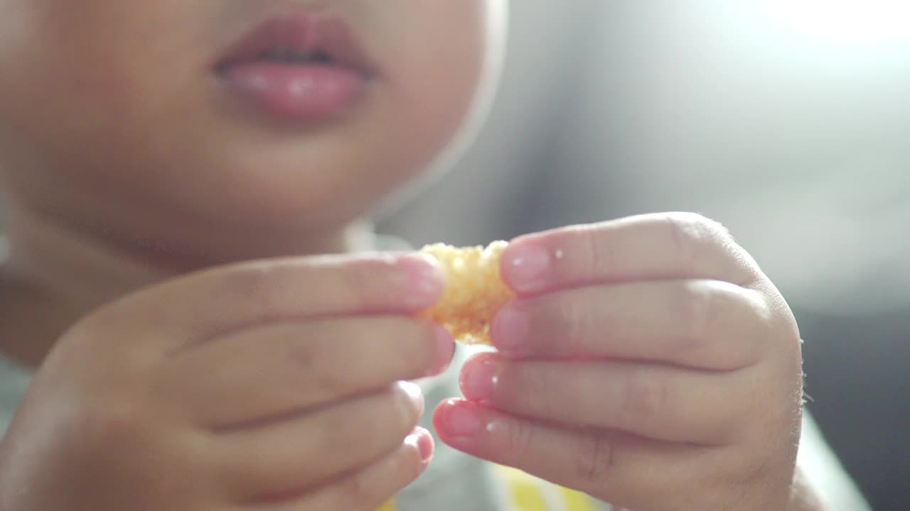 一个蹒跚学步的男孩在家用手吃一些食物视频素材