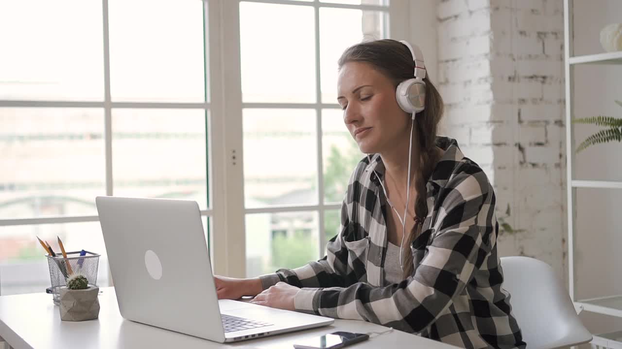 年轻的女企业家设计师听音乐耳机，同时工作在笔记本电脑。女售货员视频下载