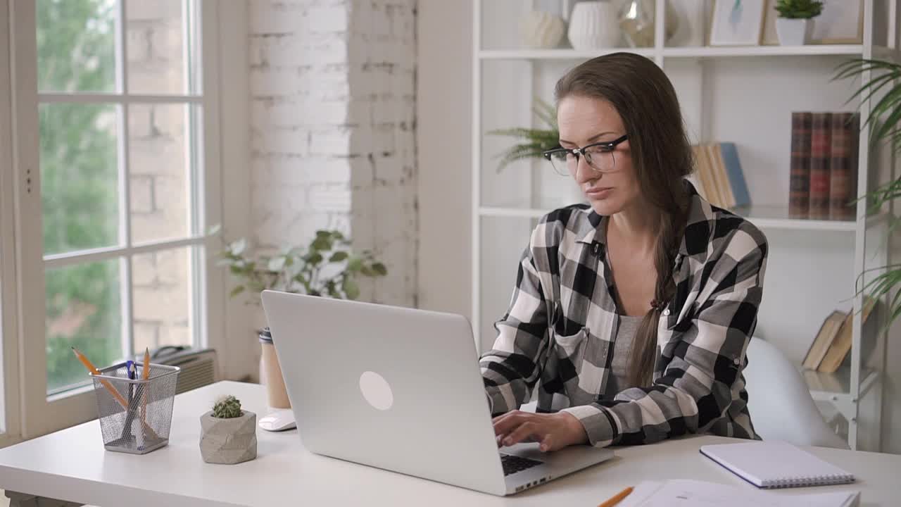 在投资明亮的公寓里，一位成功的女商人坐在桌旁用笔记本电脑工作视频下载