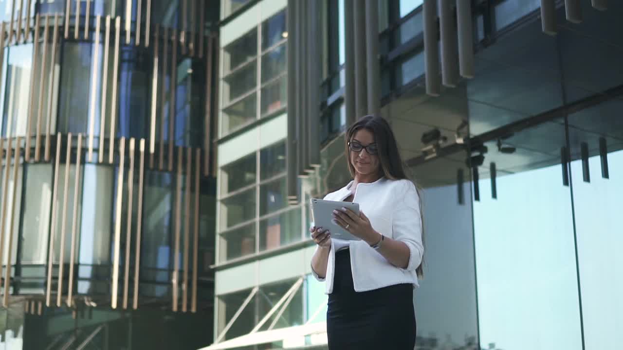 年轻漂亮的女律师正在用写字板，站在办公楼的背景上视频下载