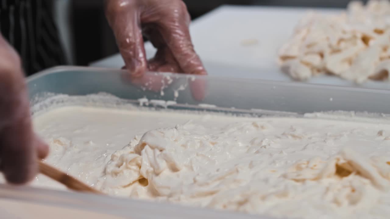 一名男子在一大桶液体中将软奶酪块与抹刀混合视频素材