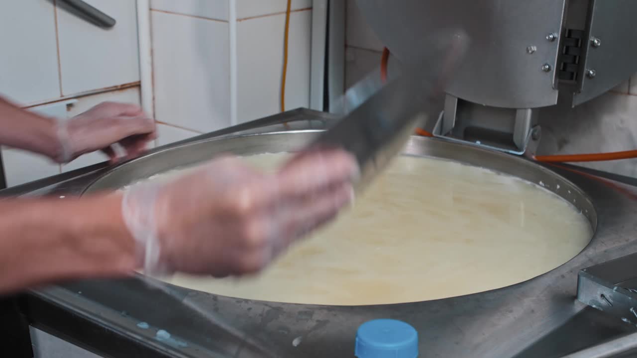奶酪生产工人用大铁板在大桶中搅拌新鲜的软奶酪视频素材