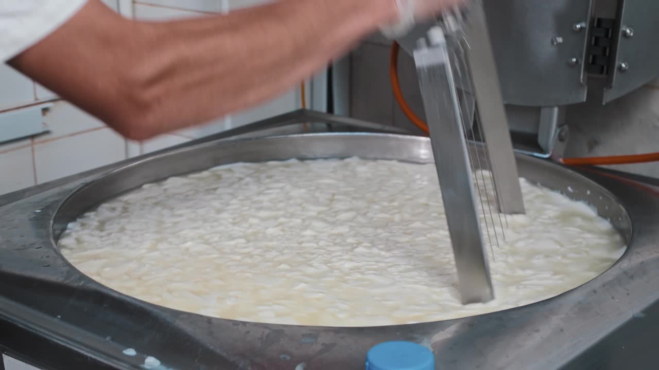 戴着手套的工人在大桶里用一把大剃刀把柔软的新鲜奶酪切成碎片视频素材