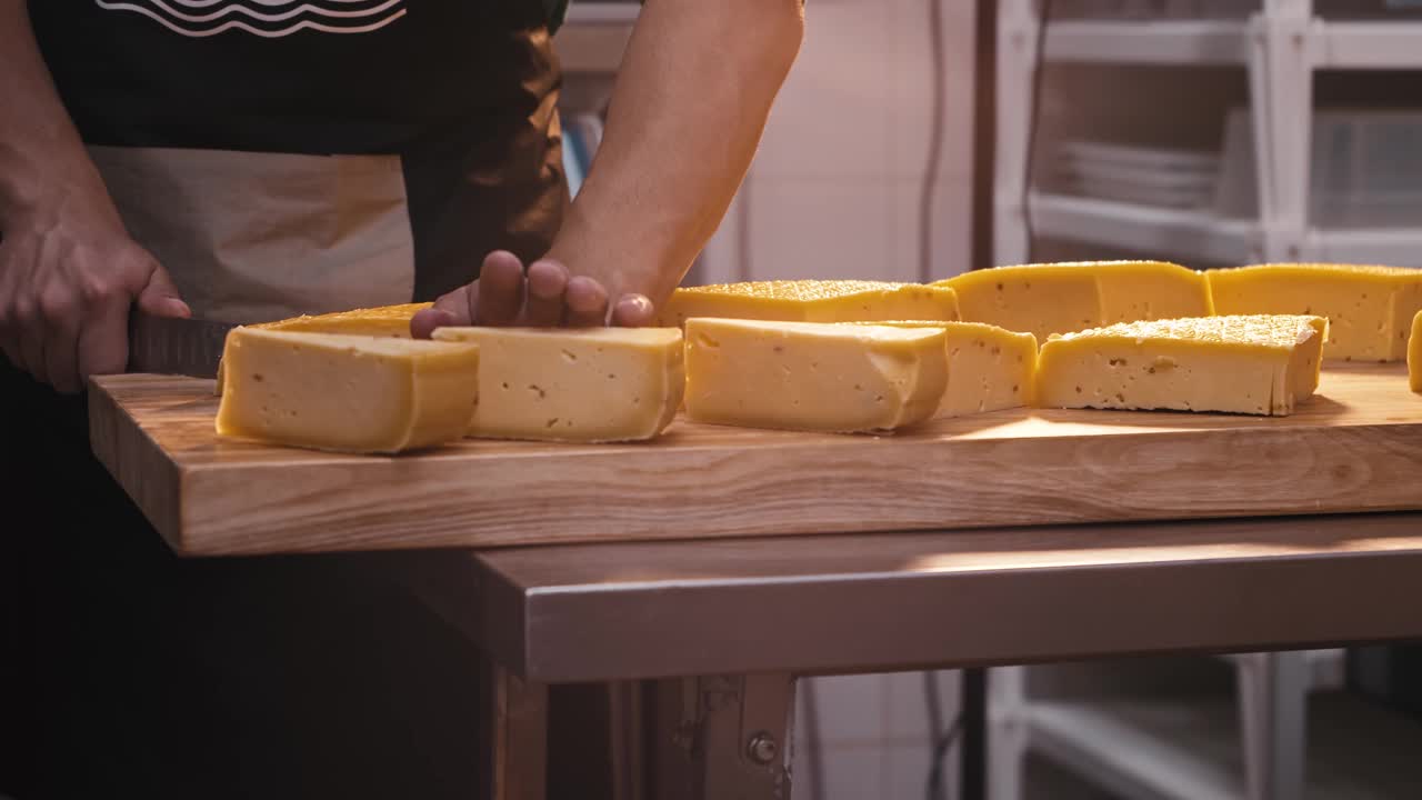 一个男人在奶酪店用刀把一个巨大的奶酪头切成碎片视频素材