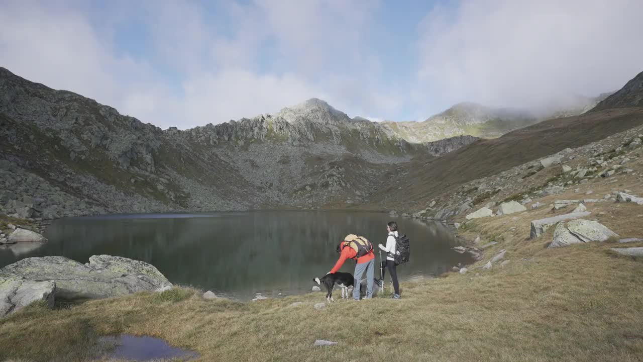 一男一女带着一只狗站在山间的湖边视频素材