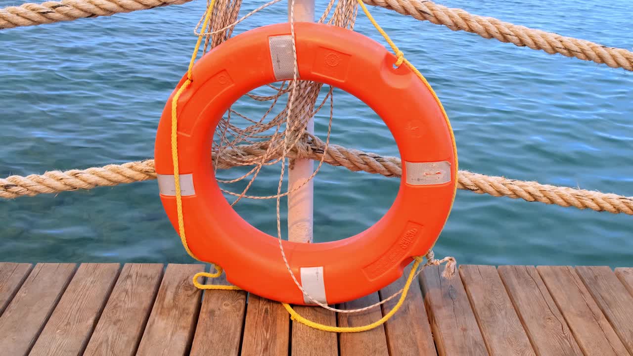 橙色的生命线和海绳在大海和蓝天的背景上。挂在一根柱子上的海缆和救生圈。救助和安全概念视频下载