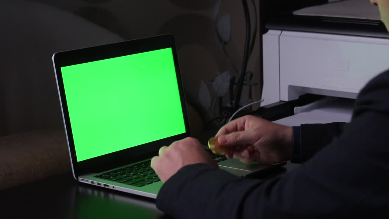 一名男子在一台绿色屏幕的笔记本电脑前工作。手中持有加密货币。Chromakey。视频素材