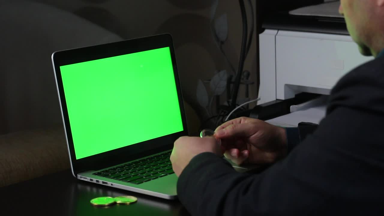 一名男子检查手中的加密货币。他把电脑放在一边，开始用绿色屏幕的笔记本电脑工作。竖起大拇指的手势。Chromakey。视频素材