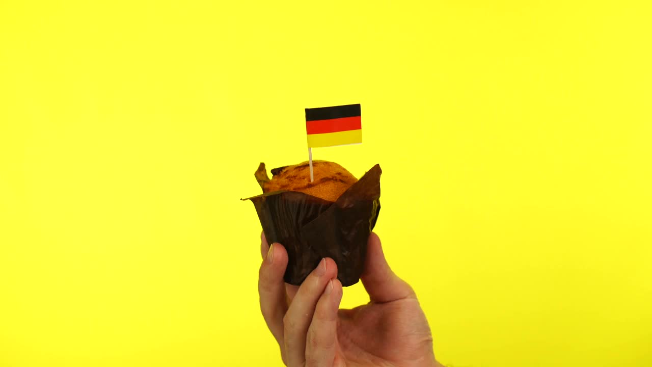 黄色背景下，男性手掌上印有德国国旗的纸杯蛋糕视频下载