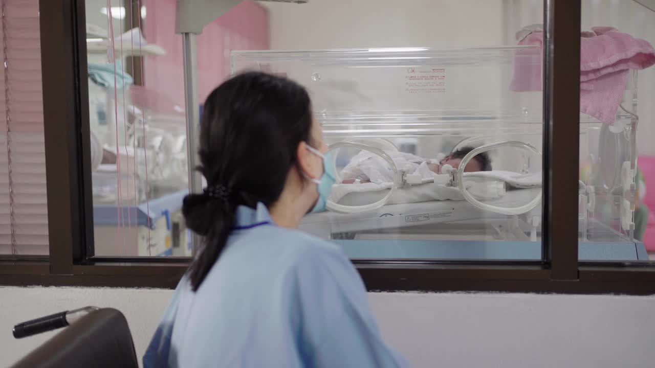 在医院里，妈妈细心地看着保温箱里的婴儿。视频素材