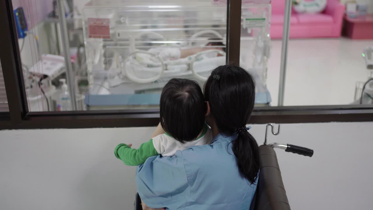 妈妈和女儿在孵化器里看着婴儿视频素材