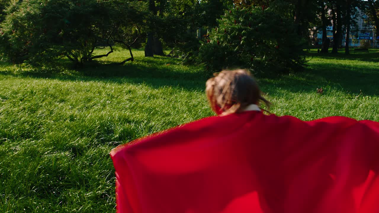 在镜头前的公园中央，一个可爱的小男孩穿着超级英雄的衣服在快速奔跑视频下载
