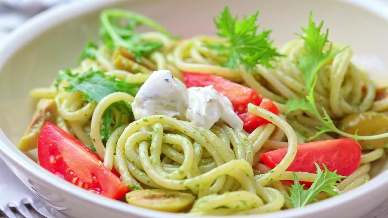 意大利通心粉配香蒜沙司，橄榄，西红柿和松子在白色碗里。视频素材