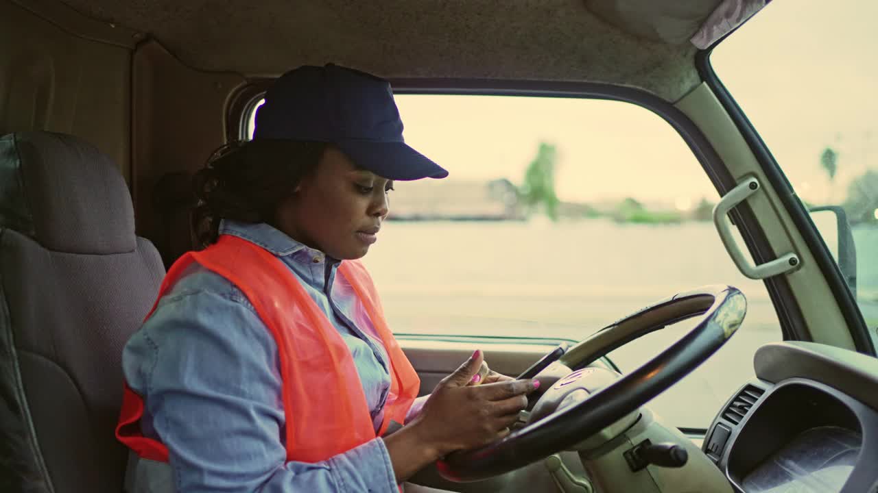 黑人女卡车司机在驾驶室检查智能手机视频素材
