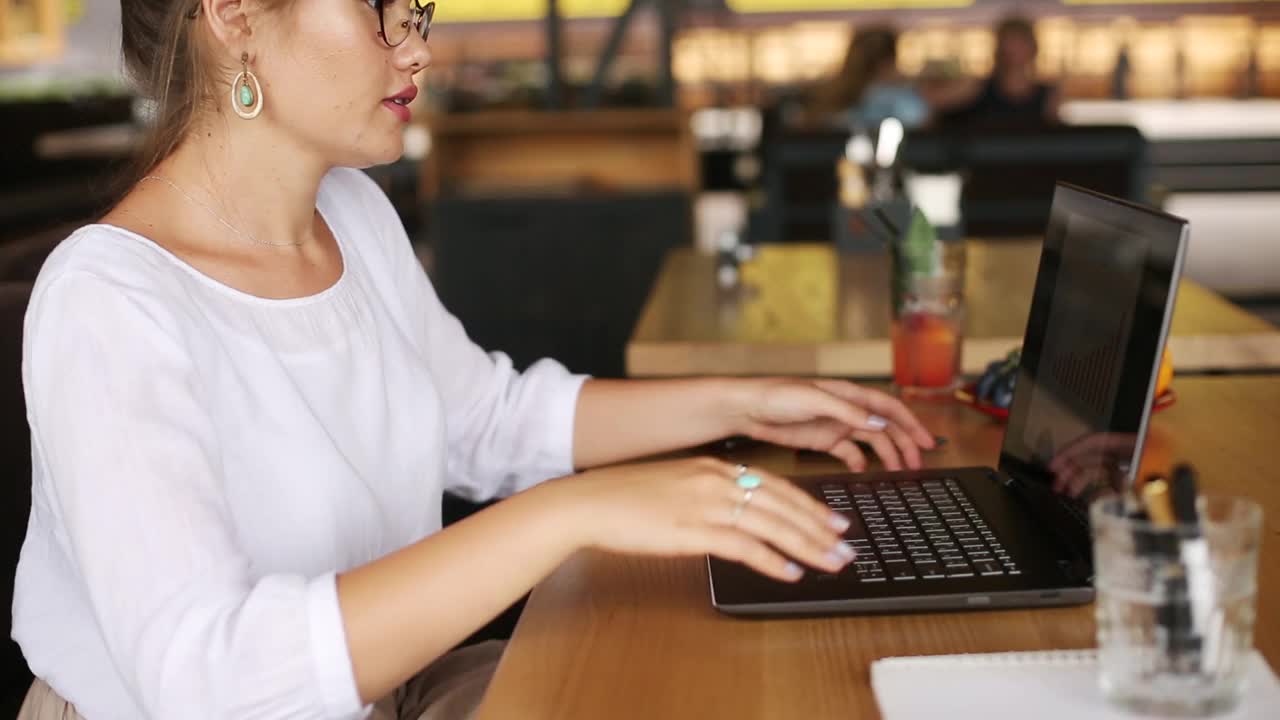 混合种族自由职业者转换笔记本电脑到平板电脑，而工作在咖啡馆。亚洲白人女商人与变压器笔记本。数码艺术家使用触摸屏二合一电脑视频素材