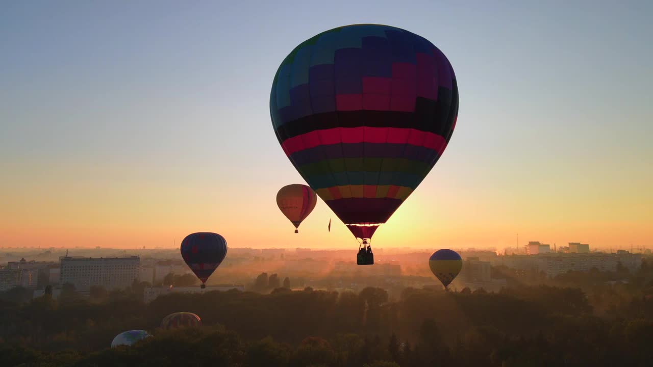 在夏季日出时，空中无人驾驶飞机在小欧洲城市的绿色公园上空飞行的彩色热气球剪影。HDR视频视频下载