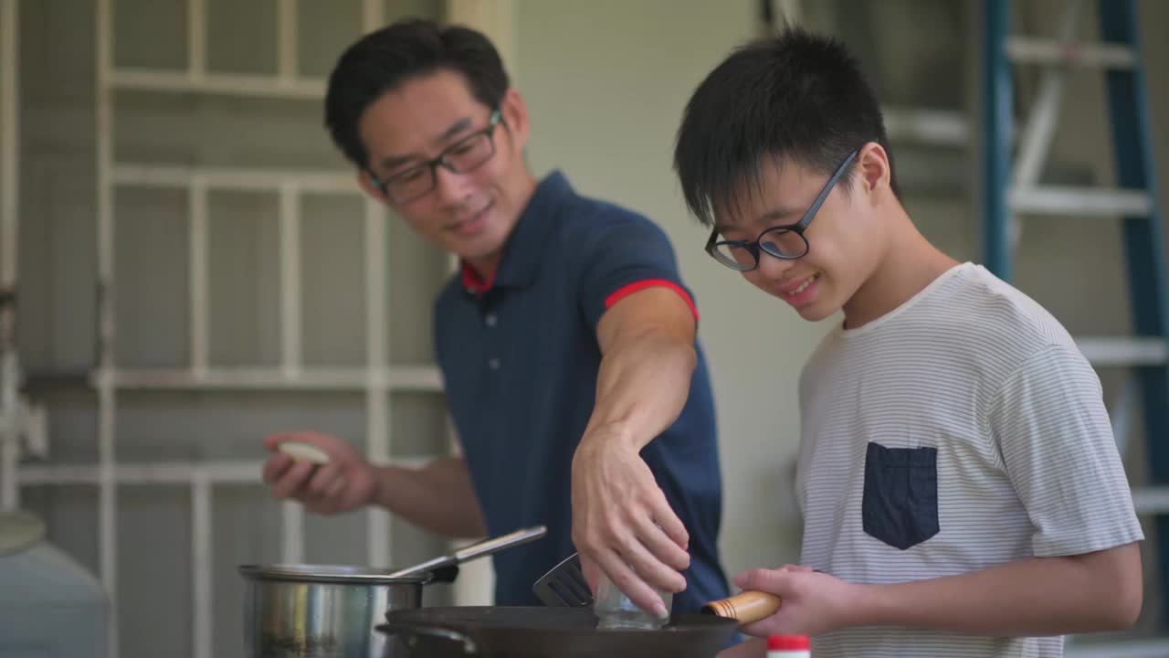 周末，一位亚洲华人父亲在自家后院的厨房教儿子做饭，准备晚餐视频下载