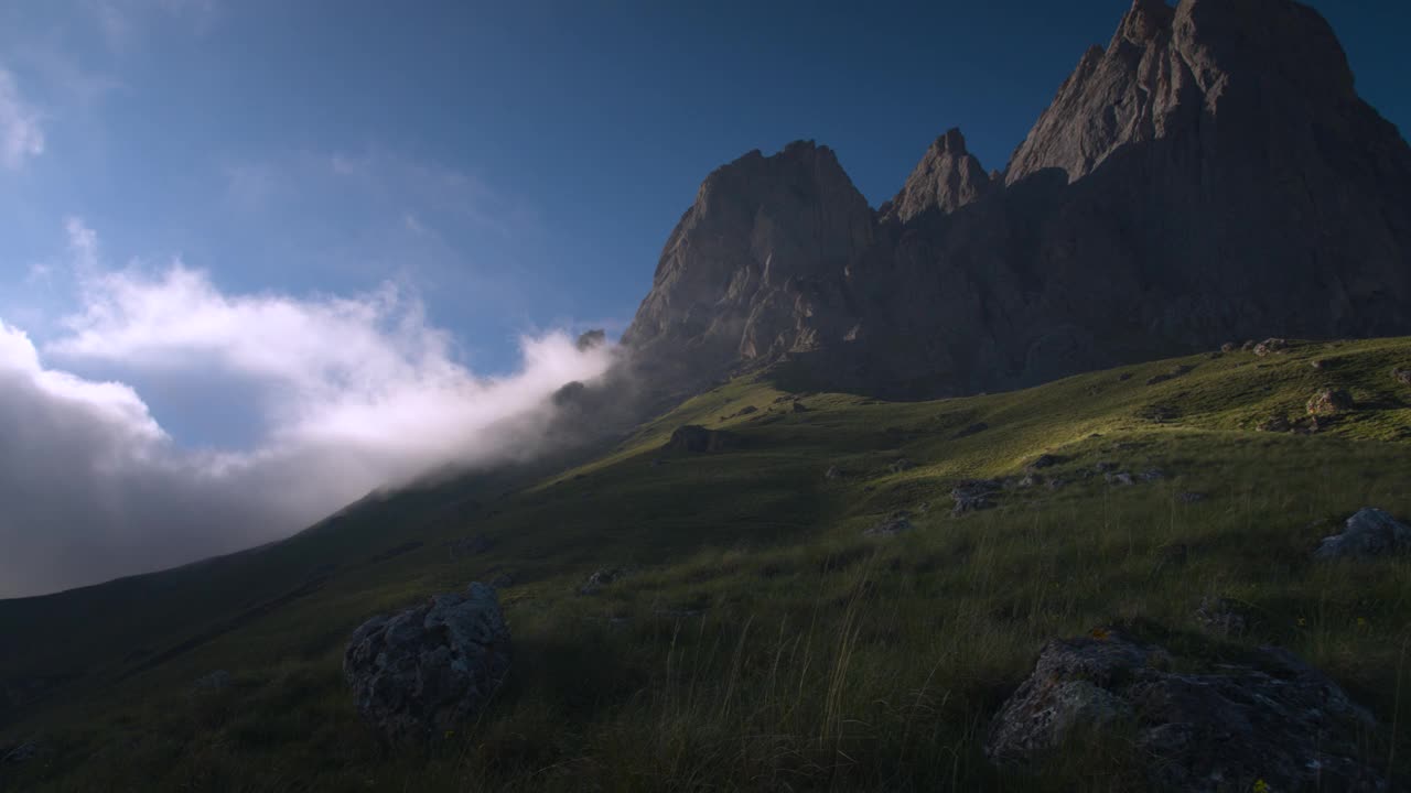 日落前的傍晚，岩石山的云朵被绿草包围的广阔动态范围的全景。来自原始视频的紧张帧视频素材
