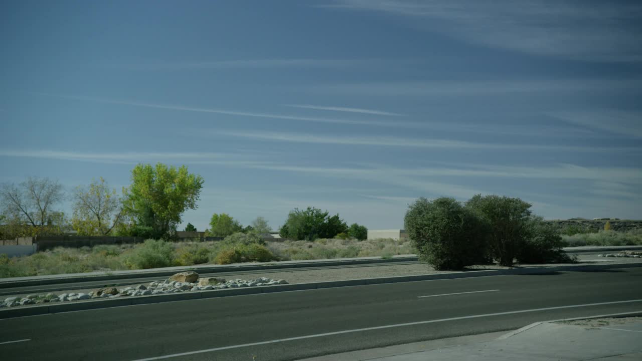 当汽车从左到右行驶时，道路的中等角度。中间有灌木和岩石可见。在bg中可见的树。农村地区。蓝色的天空。视频素材