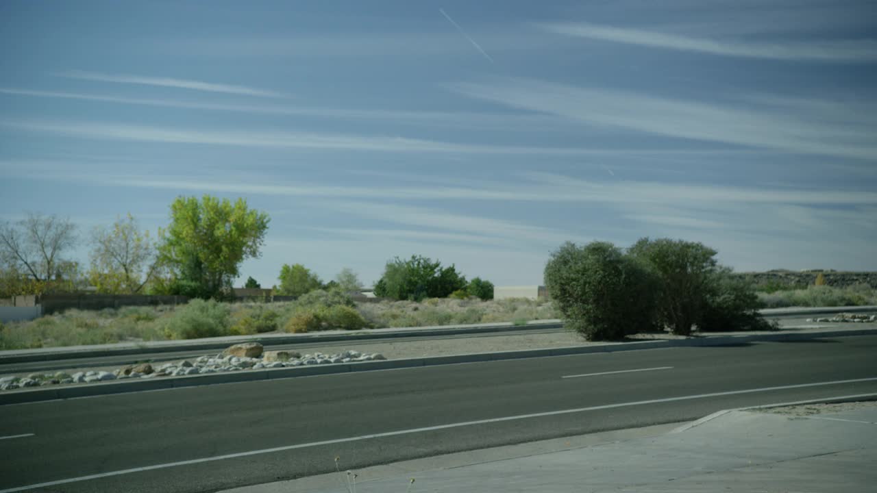 当汽车在两个方向上行驶时，道路的角度适中。中间有灌木和岩石可见。在bg中可见的树。农村地区。蓝色的天空。视频素材